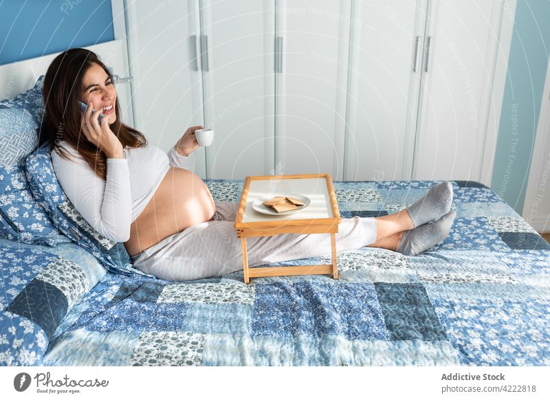 Glückliche schwangere Frau, die frühstückt und mit ihrem Smartphone spricht Frühstück Bett Morgen Schwangerschaft reden sprechen Telefonanruf heimwärts Gerät
