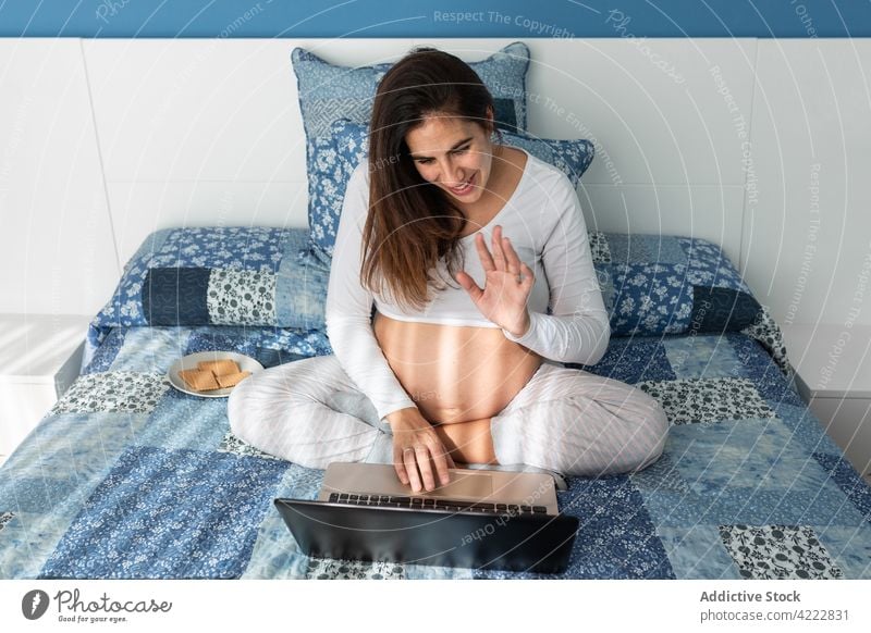 Schwangere Frau im Videochat auf dem Laptop schwanger Videoanruf Video-Chat Wellenhand Gruß Hallo Schwangerschaft reden heimwärts Lächeln Gespräch online Glück