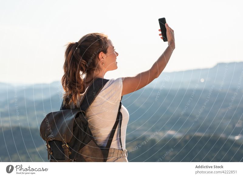 Zufriedene weibliche Reisende, die ein Selfie auf einer üppigen Hügelkuppe macht Frau Smartphone Bergkuppe Natur Selbstportrait fotografieren Inhalt Wanderer