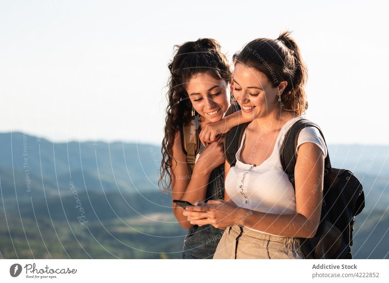 Fröhliche Frauen mit Smartphone in sonnigem, hügeligem Terrain benutzend Freund Zusammensein Glück Natur Reisender heiter Apparatur jung Browsen Gerät Telefon