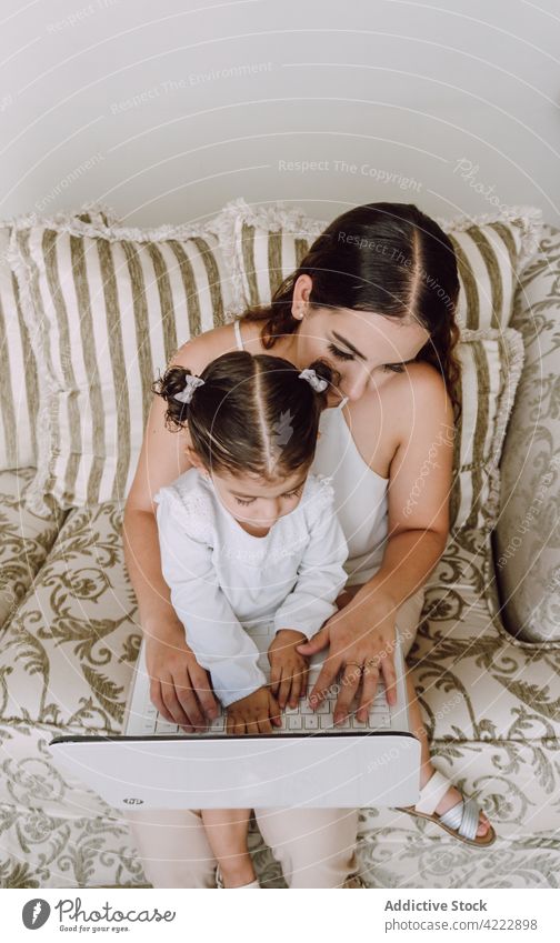 Mutter und Tochter schauen einen Film auf dem Laptop Kind zuschauen Karikatur heimwärts wenig Frau Zusammensein ethnisch Sofa benutzend Mädchen Apparatur