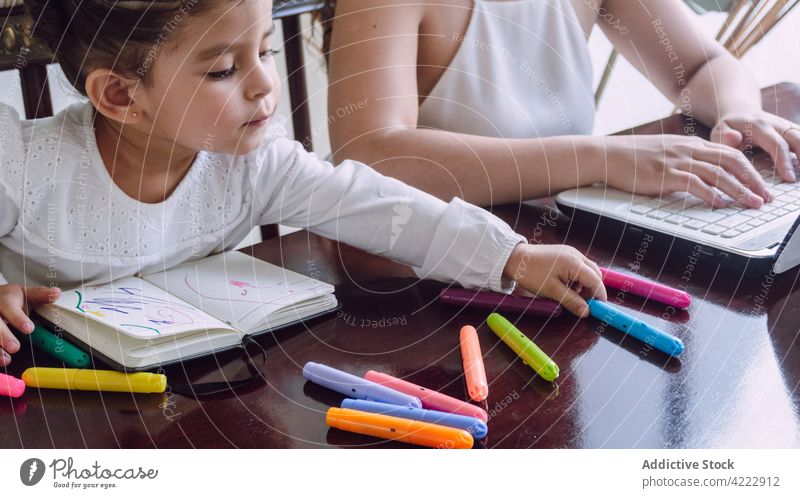 Crop Mutter Surfen Laptop und Kind Zeichnung zu Hause Zusammensein Kinderbetreuung Markierung zeichnen Filzstift heimwärts kreativ Bildung Notebook Tisch wenig
