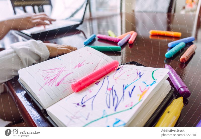 Crop Mutter und Kind am Tisch mit Notizbuch und Stiften Notebook Filzstift zeichnen Streuung unordentlich Zeichnung Bild Kinderbetreuung sitzen Zusammensein