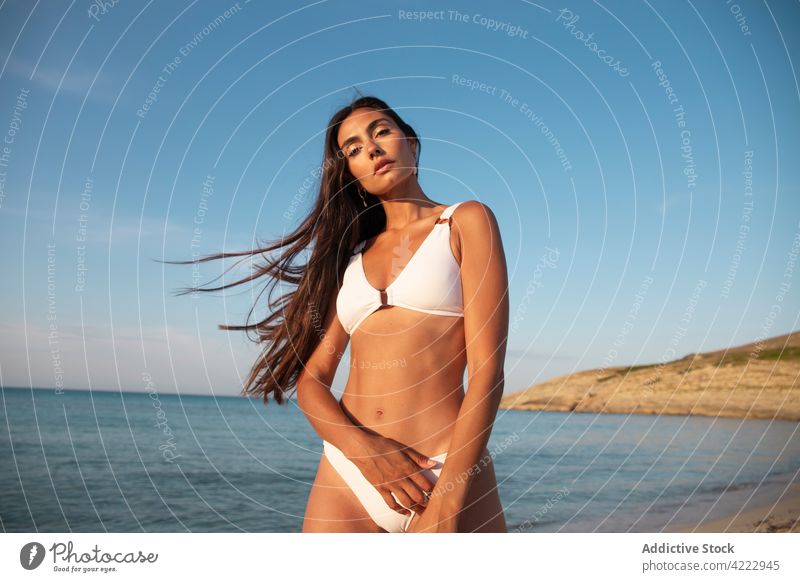 Modell im Badeanzug am Strand gegen das Meer MEER Körper Badebekleidung feminin selbstbewusst Meereslandschaft Frau Porträt Blauer Himmel sandig Natur wolkig