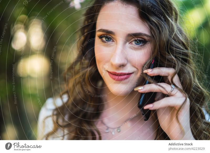 Lächelnde junge Frau benutzt ihr Smartphone in einem üppigen Park sprechend benutzend Garten Inhalt Stil sorgenfrei Mobile attraktiv schön heiter Apparatur