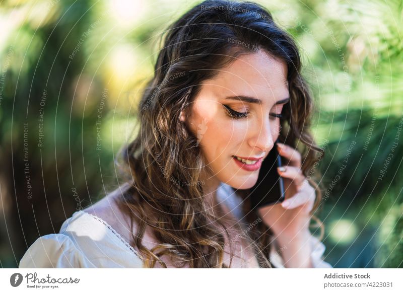Lächelnde junge Frau benutzt ihr Smartphone in einem üppigen Park sprechend benutzend Garten Inhalt Stil sorgenfrei Mobile attraktiv schön heiter Apparatur
