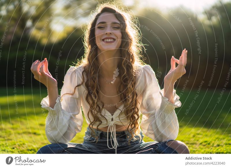 Lächelnde Frau meditiert in Lotus-Pose im sonnigen Park meditieren pflanzlich Yoga Augen geschlossen Achtsamkeit Asana padmasana Gelassenheit Zen Natur