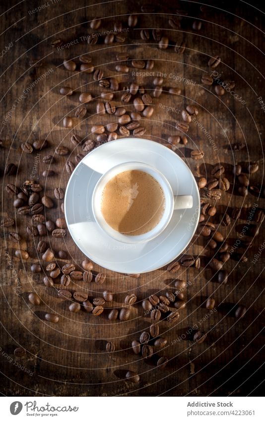 Tasse mit aromatischem Espresso zwischen Kaffeebohnen auf braunem Hintergrund Bohne Heißgetränk Getränk schäumen Aroma natürlich Untertasse verschütten trocknen