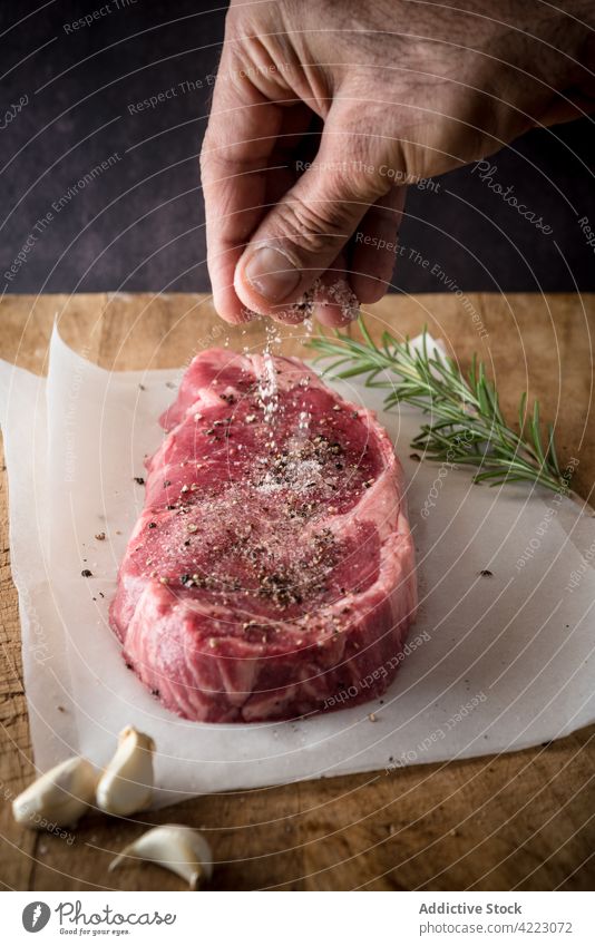 Crop-Chefkoch salzt rohes Rindersteak auf Pergament Küchenchef Gewürz Steak Rindfleisch Fleisch Protein kulinarisch Rezept Mann Prozess Rosmarin Zweig frisch