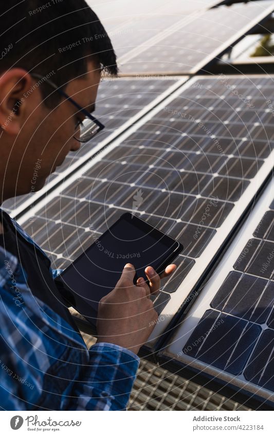 Fokussierter ethnischer Ingenieur mit Tablet in der Nähe eines Solarpanels Mann solar Kraft Tablette benutzend Photovoltaik Panel Techniker Arbeit ernst