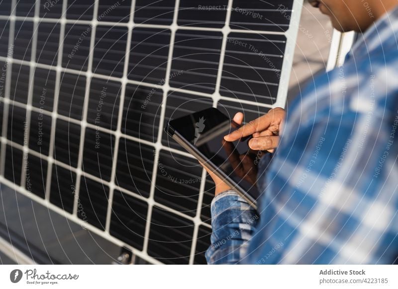 Anonymer ethnischer Ingenieur benutzt Tablet in der Nähe eines Solarpanels Mann solar Kraft Tablette benutzend Photovoltaik Panel Fokus Techniker Arbeit Station