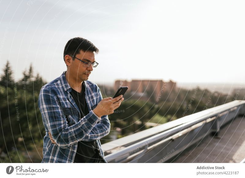 Fokussierter Mann mit Smartphone auf dem Dach benutzend Browsen Dachterrasse Vorstadt Apparatur Konzentration Telefon Nachricht lässig modern Surfen online