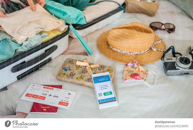 Frau bereitet Koffer für Urlaub und Handy mit covid grünem Pass vor Covid-Pass digitaler Gesundheitspass Grüner Pass Hände vorbereitend auf dem Bett Feiertag