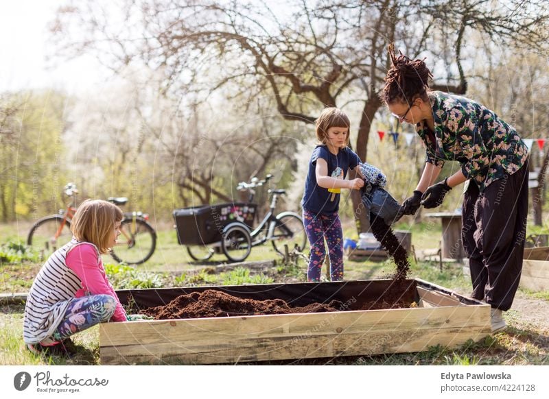 Mutter mit zwei kleinen Töchtern bei der Gartenarbeit im städtischen Gemeinschaftsgarten städtischer Garten Umweltschonung nachhaltiger Lebensstil hausgemacht