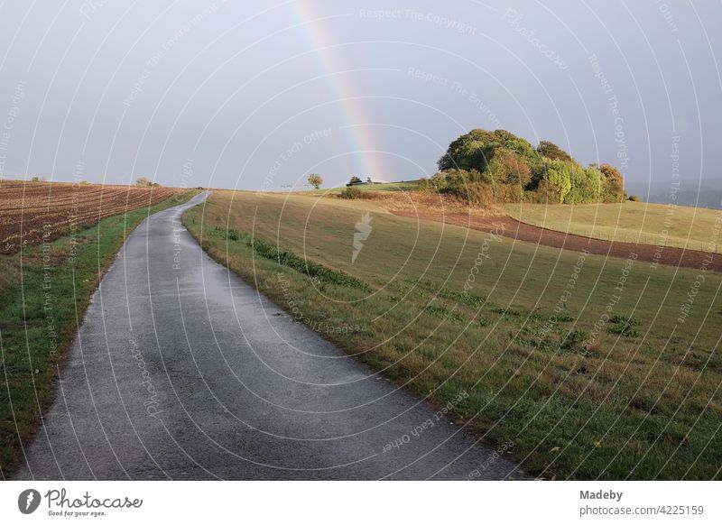 Einsame Straße durch Wiesen und Felder nach dem Regen mit schönem Regenbogen am Horizont in Gembeck am Twistetal im Kreis Waldeck-Frankenberg in Hessen