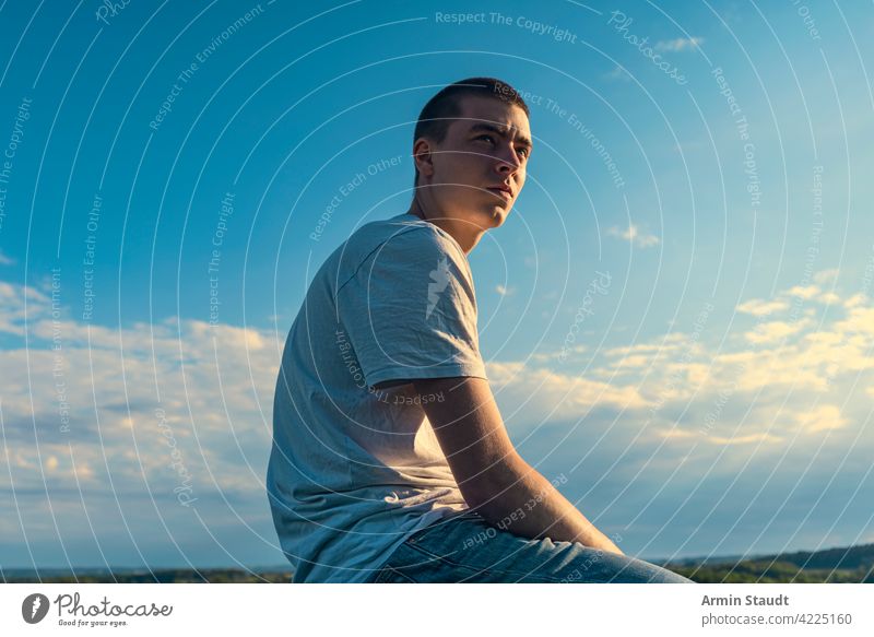 sitzender junger Mann schaut in die Ferne in einer schönen Landschaft Sitzen Blick Himmel blau Sommer im Freien PKW Sonnenuntergang Natur Sonnenlicht