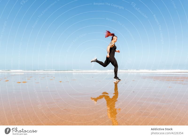 Schneller Läufer joggt am Sandstrand während des Trainings Jogger laufen Meeresufer Sport Herz Aktivität Tattoo Frau Reflexion & Spiegelung Sportlerin Übung