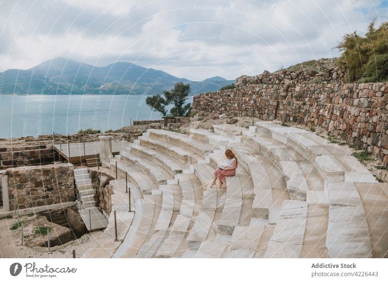 Unbekannte Frau liest ein Buch und sitzt auf den Stufen eines alten Theaters lesen antik historisch Meeresufer Erbe Treppe Fernweh Plaka Milos Griechenland