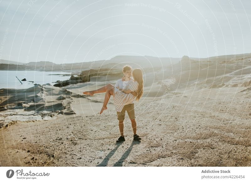 Mann trägt seine Freundin an der steinigen Meeresküste Paar führen Meeresufer rau felsig Zusammensein Partnerschaft romantisch jung Liebe malerisch attraktiv