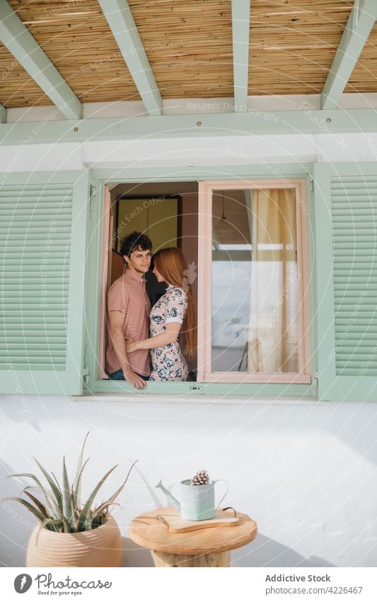 Junges Paar, das sich in der Nähe des Fensters in einem kleinen Häuschen umarmt Umarmen Haus Angebot verliebt Cottage Dorf Partnerschaft romantisch sonnig