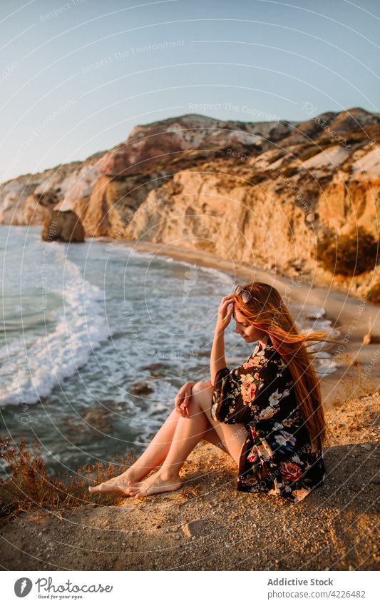 Frau sitzt auf einer malerischen Felsenküste Meeresufer felsig Natur Haare berühren Resort Küstenlinie feminin Klippe fyriplaka bewundern Reisender Stil Milos