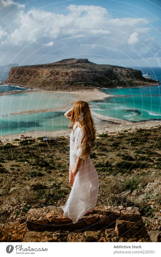 Unerkennbare Frau steht auf einem steinigen Aussichtspunkt vor azurblauem Meer Balos Strand Haare berühren Bergkuppe Strandbekleidung Resort Paradies malerisch