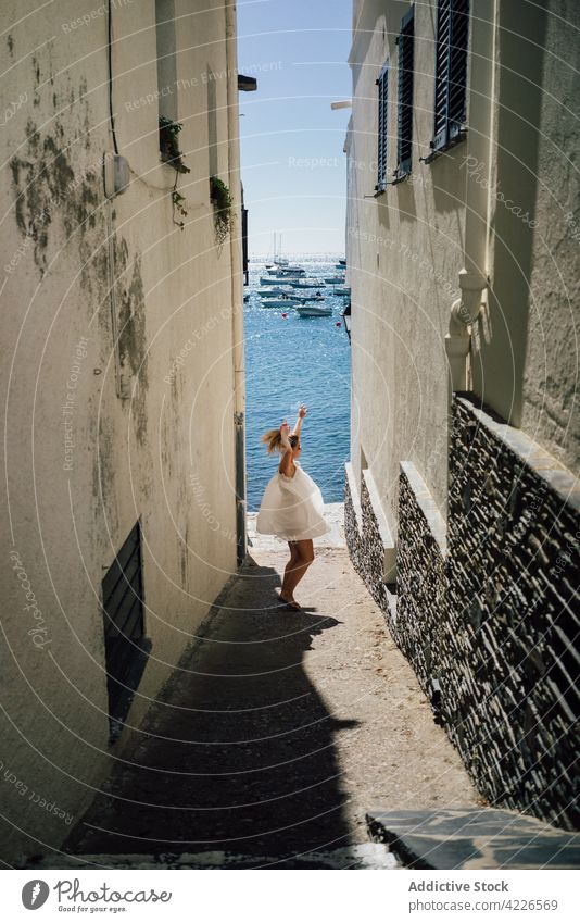 Unbekannter aufgeregter Reisender, der sich in der Stadt am Meer vergnügt Tourist Tanzen Spaß haben Arme hochgezogen Urlaub Architektur Gebäude Straße MEER Frau
