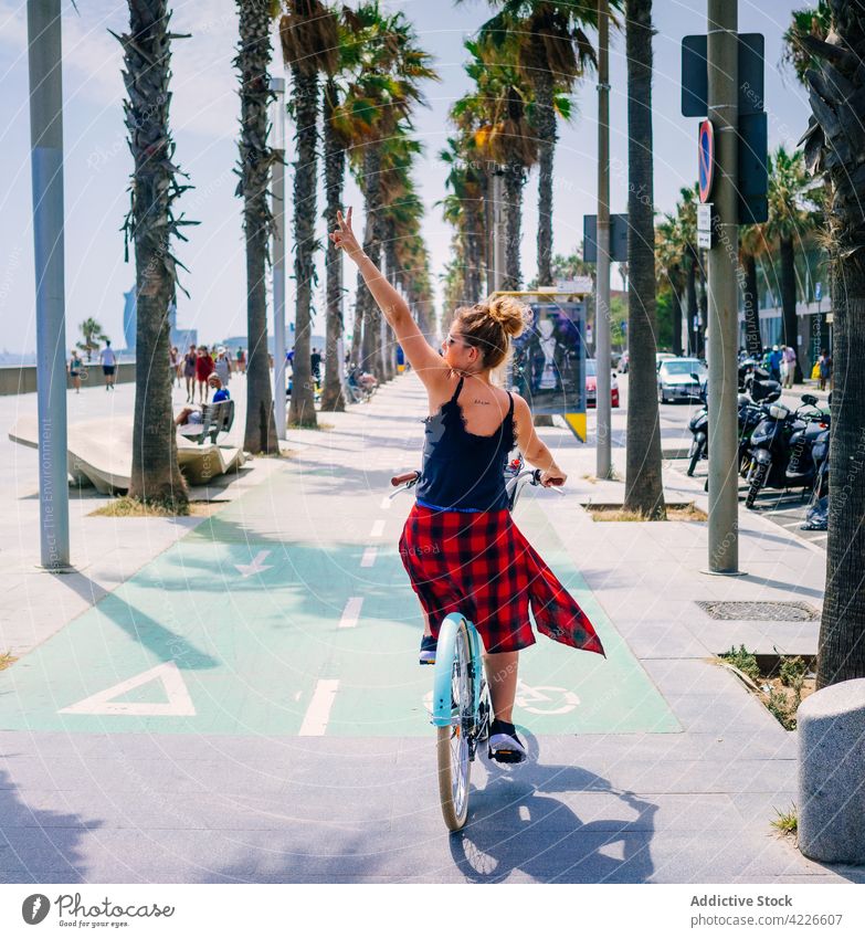 Radfahrer auf dem Fahrrad und zeigt die Friedensgeste auf dem städtischen Bürgersteig Biker Mitfahrgelegenheit zwei Finger Route cool Arm angehoben Großstadt