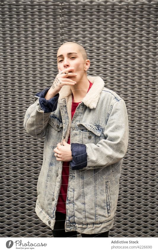 Transsexuelle Person mit Tattoo raucht Zigarette auf grauem Hintergrund Transgender Rauch selbstbewusst eitel Individualität cool Streetstyle Porträt queer