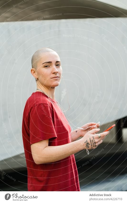 Lesbische Frau mit Smartphone und Tattoos auf einer Straße in der Stadt lesbisch Kopfhörer akzeptieren zuhören Musik Großstadt Porträt benutzend Apparatur Gerät