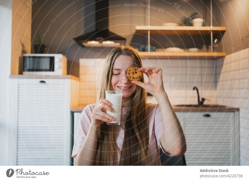 Lächelnde Frau, die ihr Auge mit einem Haferflockenkeks in der Küche bedeckt Auge abdecken Keks melken Frühstück heiter süß Leckerbissen Augen geschlossen