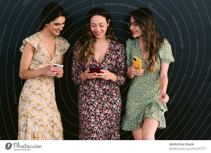 Glückliche Freundinnen in schicken Kleidern mit Smartphones auf dem Bürgersteig bester Freund Stil trendy Freundschaft feminin Frauen Straßenbelag benutzend