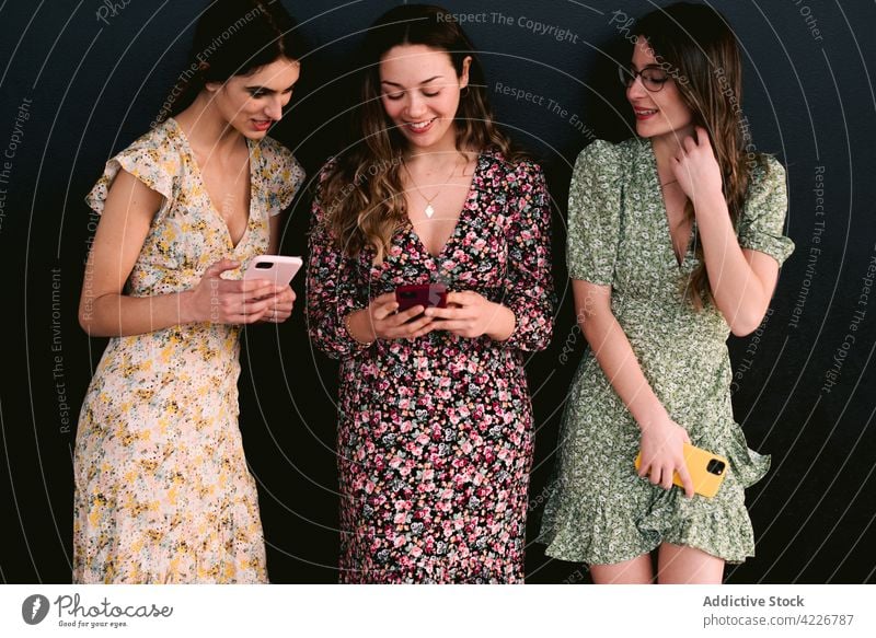 Glückliche Freundinnen in schicken Kleidern mit Smartphones auf dem Bürgersteig bester Freund Stil trendy Freundschaft feminin Frauen Straßenbelag benutzend