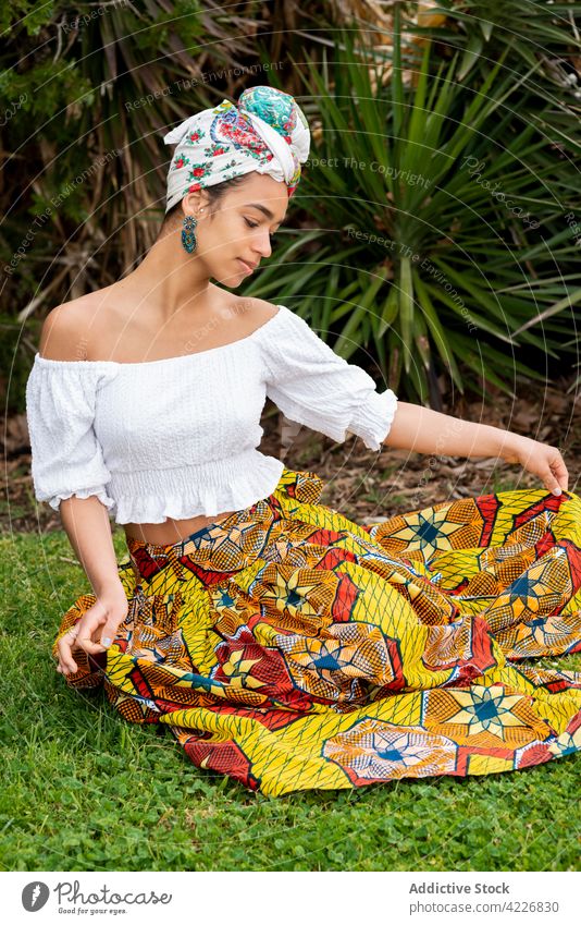 Schwarze Frau in traditioneller Kleidung auf Rasen heiter Ornament Stil freundlich tropisch Handfläche Garten Porträt Afrikanisch Inhalt Lächeln froh Rock Bluse