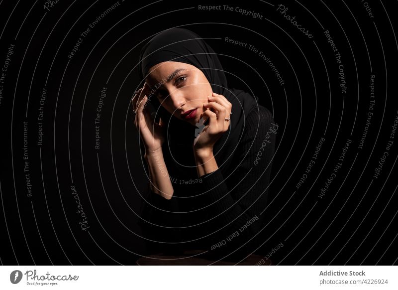 Wunderschöne muslimische Frau mit schwarzem Kopftuch, die ihr Gesicht berührt Outfit Hijab traumhaft Stil Gesicht berühren Körperhaltung Kultur Vorschein