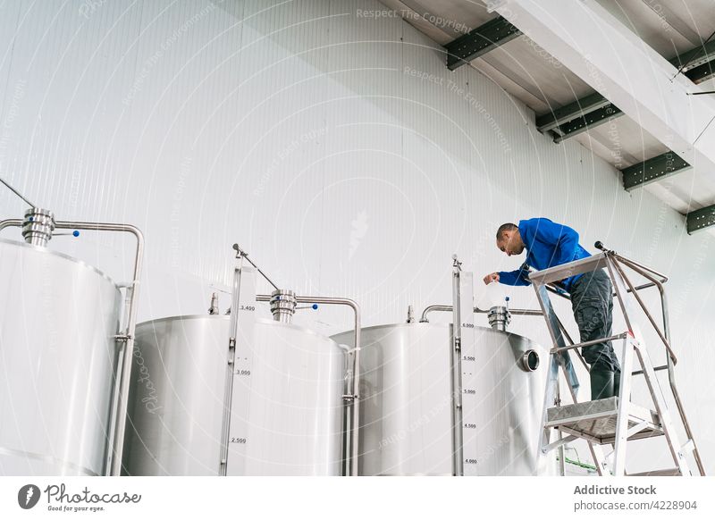 Bierbrauer auf einer Leiter beim Füllen eines Gärbehälters in einer Bierfabrik Brauer besetzen Tank Fermentation Arbeit Industrie Mann Kleinunternehmen