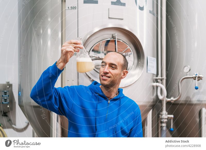 Lächelnder Brauer mit Würze im Kolben in der Fabrik Flasche fermentiert Analyse schäumen Mann Kleinunternehmen Porträt Inszenierung Tank Fermentation Arbeit