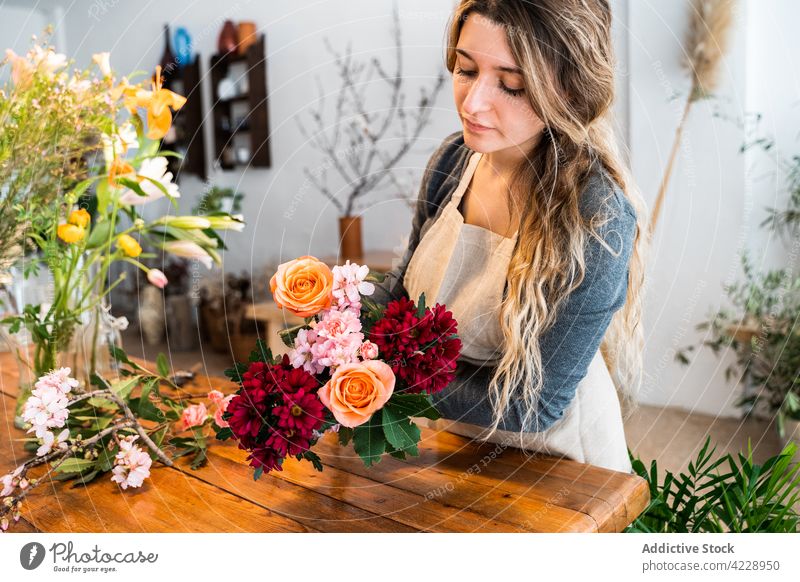 Fokussierte junge Blumenhändlerin, die eine Komposition mit verschiedenen frischen Blumen erstellt Frau Blumenstrauß Roséwein Arbeit Pflanze geblümt