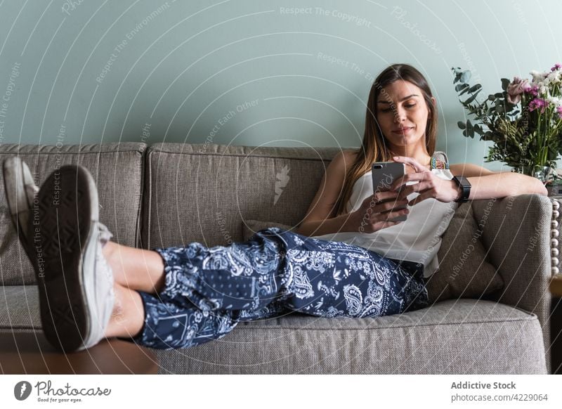 Frau, die zu Hause auf dem Sofa mit ihrem Smartphone chattet plaudernd freie Zeit Wochenende Internet Beine gekreuzt benutzend Apparatur Gerät Lifestyle