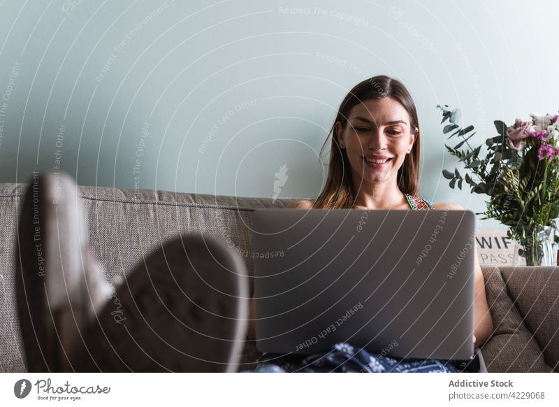 Lächelnde Frau mit Laptop auf der Couch zu Hause Internet online Inhalt Sofa benutzend Apparatur Gerät interagieren heiter Zeit verbringen Wochenende Netbook