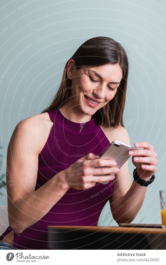 Fröhliche erwachsene Frau, die in einem Haus auf einem unscharfen Hintergrund auf ihrem Mobiltelefon surft Smartphone Zahnfarbenes Lächeln herzlich feminin