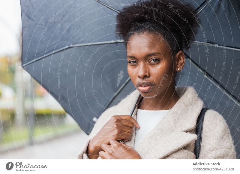 Stilvolle schwarze Frau mit Regenschirm steht auf der Straße Oberbekleidung trendy Outfit Streetstyle cool modisch Vorschein Aussehen Großstadt modern