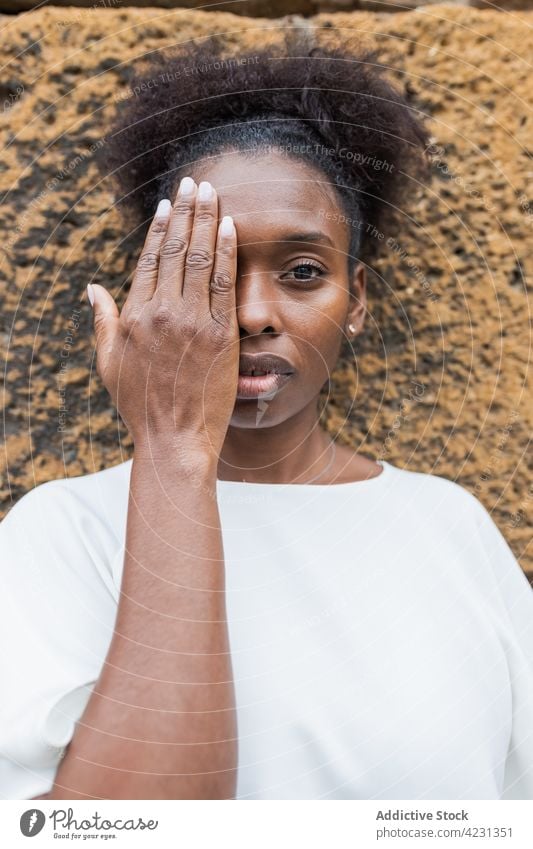Emotionslose schwarze Frau, die ihr halbes Gesicht mit der Hand bedeckt Tierhaut Deckblatt Augen abdecken Blick Windstille emotionslos Körperhaltung Vorschein