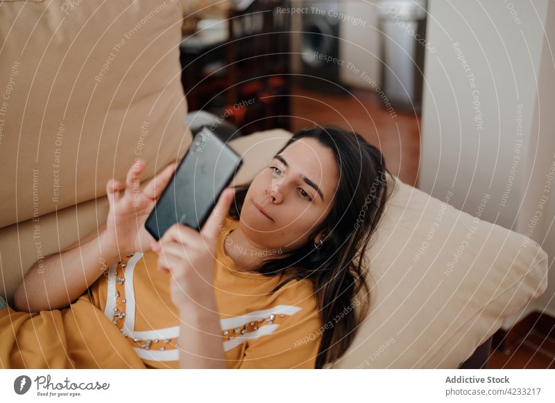 Frau, die zu Hause auf dem Sofa mit ihrem Smartphone chattet plaudernd Internet benutzend Apparatur Gerät Lifestyle liegend Funktelefon Glück Textnachrichten
