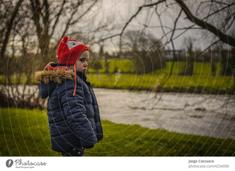 Zwei Jahre altes Mädchen, das über einen Fluss in einer ländlichen irischen Umgebung im Freien schaut. Gekleidet in Winterkleidung, großen Mantel und warme Mütze.
