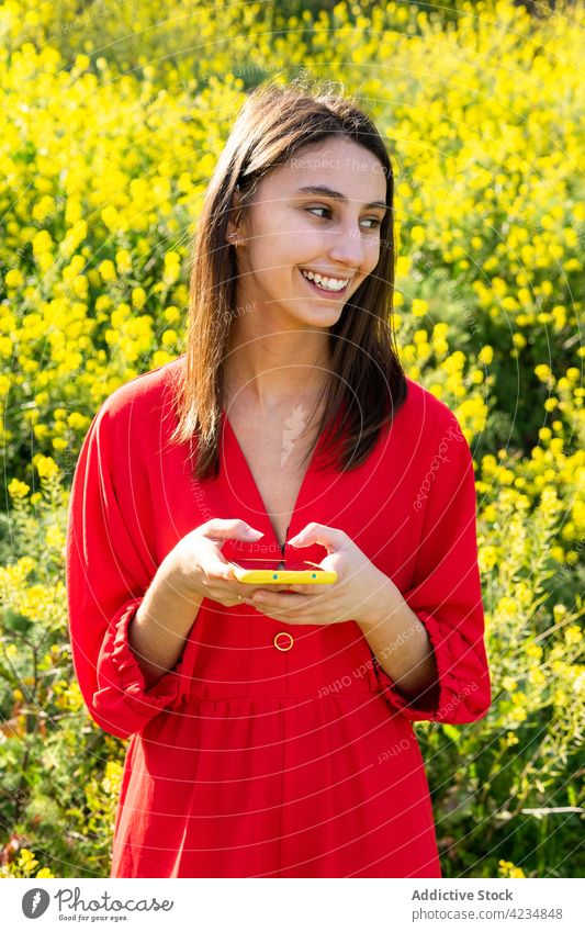 Lächelnde Frau, die im Sommer auf einem Feld mit ihrem Smartphone chattet plaudernd Freizeit Wochenende Landschaft Porträt benutzend Apparatur Gerät Funktelefon