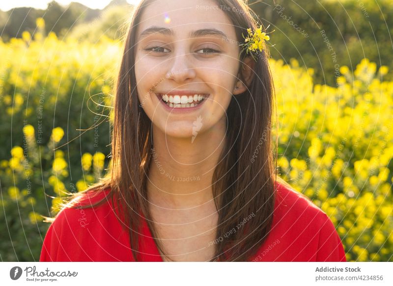 Crop glückliche Frau mit blühenden Blume im Haar in der Sonne Zahnfarbenes Lächeln offen freundlich Blüte Feld Landschaft Sonnenschein Porträt Sommer Glück