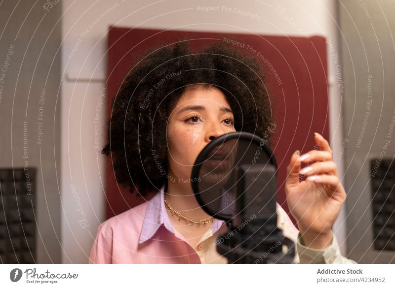Afroamerikanischer Sänger, der im Aufnahmestudio ein Lied ins Mikrofon singt Gesang Aufzeichnen Musik Hand an der Hüfte professionell Atelier Frau Sängerin