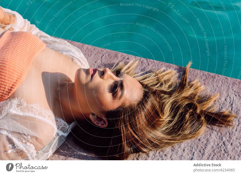 Reisende mit Ohrringen, die sich während der Reise am Pool ausruhen Tourist wehmütig feminin allein Urlaub Ausflug reflektierend Beckenrand Frau Porträt