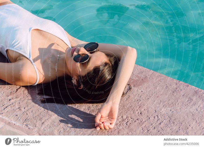 Sinnliche Touristin im Badeanzug, die sich am Swimmingpool ausruht Frau Lügen Pool Mode Stil sinnlich Sonnenbrille feminin Körper Urlaub reisen ruhen